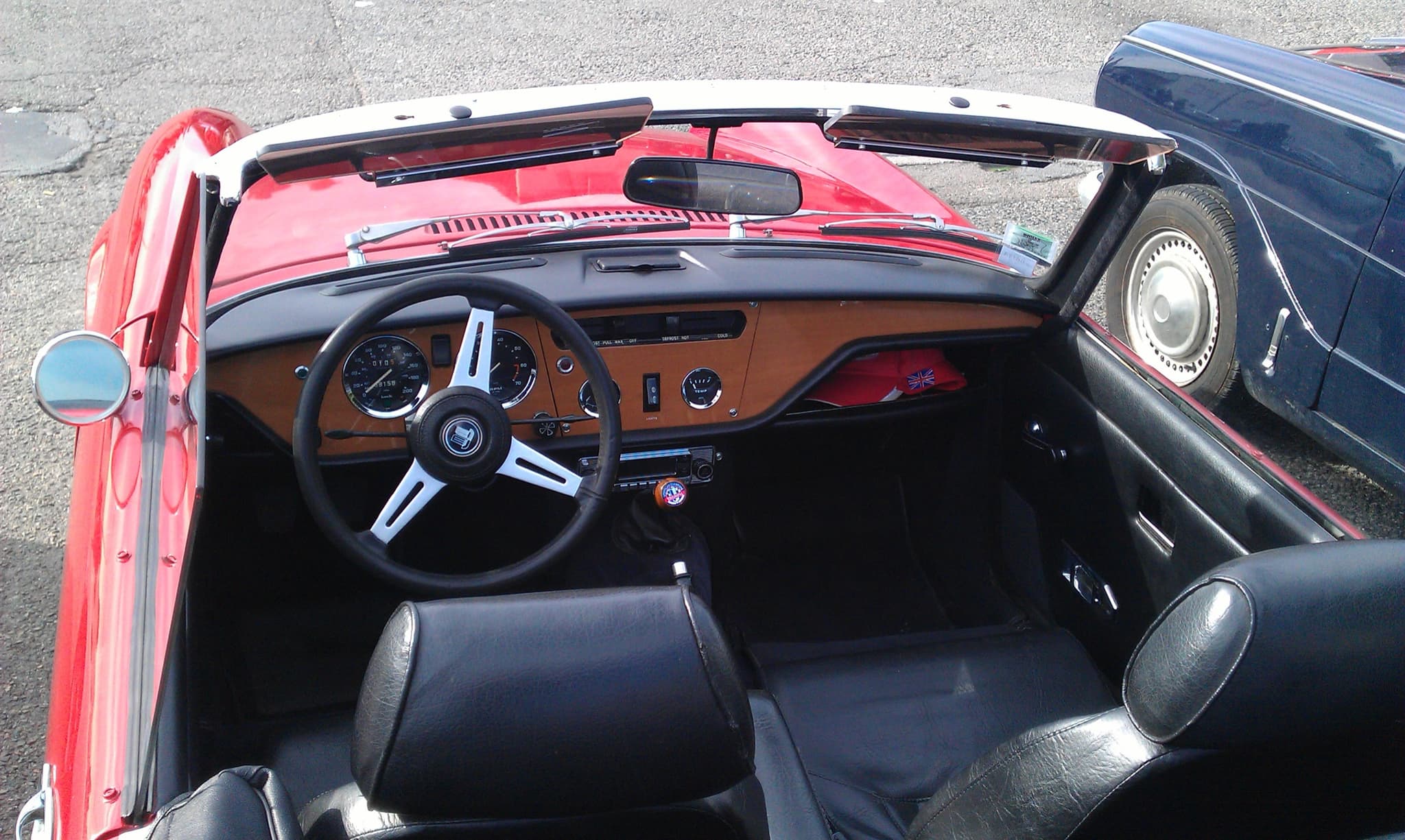 A red Spitfire cockpit from above, with a wood fascia, instruments ahead of the driver and black seats with headrests. Opens a larger view
