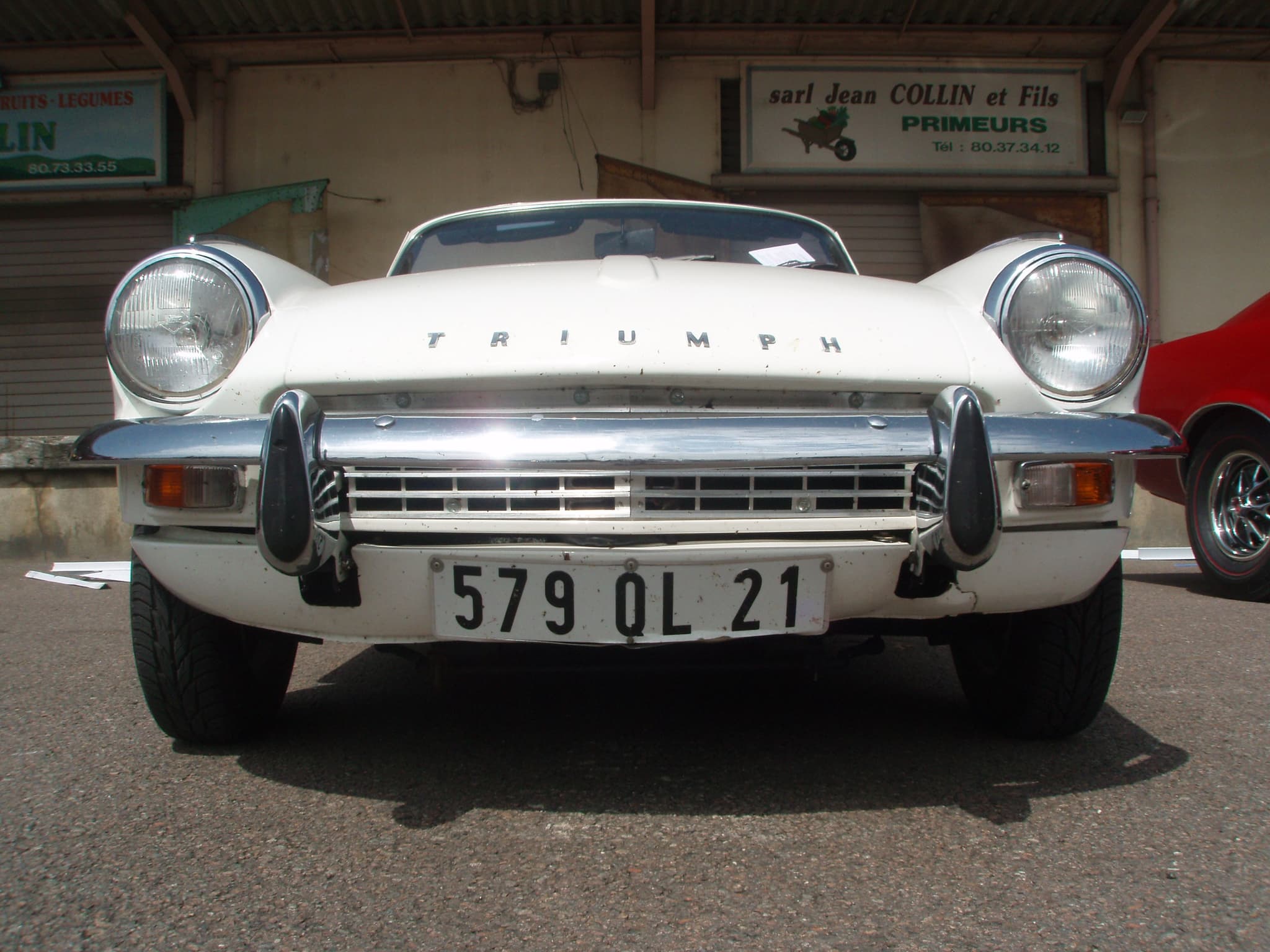 A white Spitfire Mk III square on from the front, its chrome bumper crossing the grille, outside closed shopfronts.