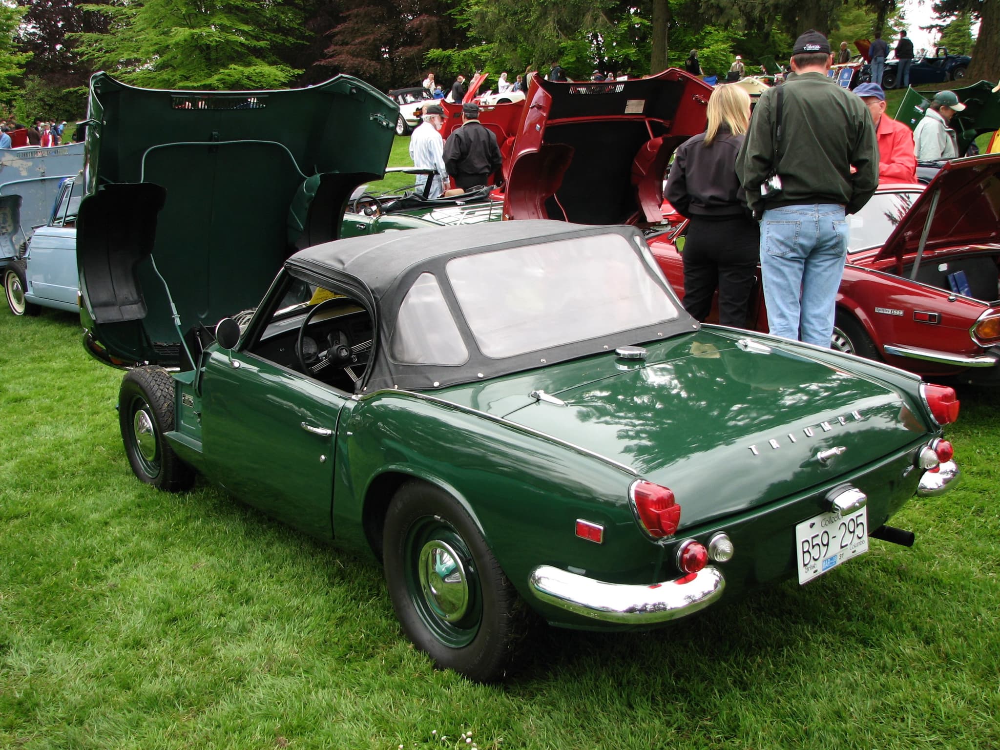 A dark green Spitfire Mk III with its hood up and bonnet raised, seen from behind on a show-field lawn. Opens a larger view
