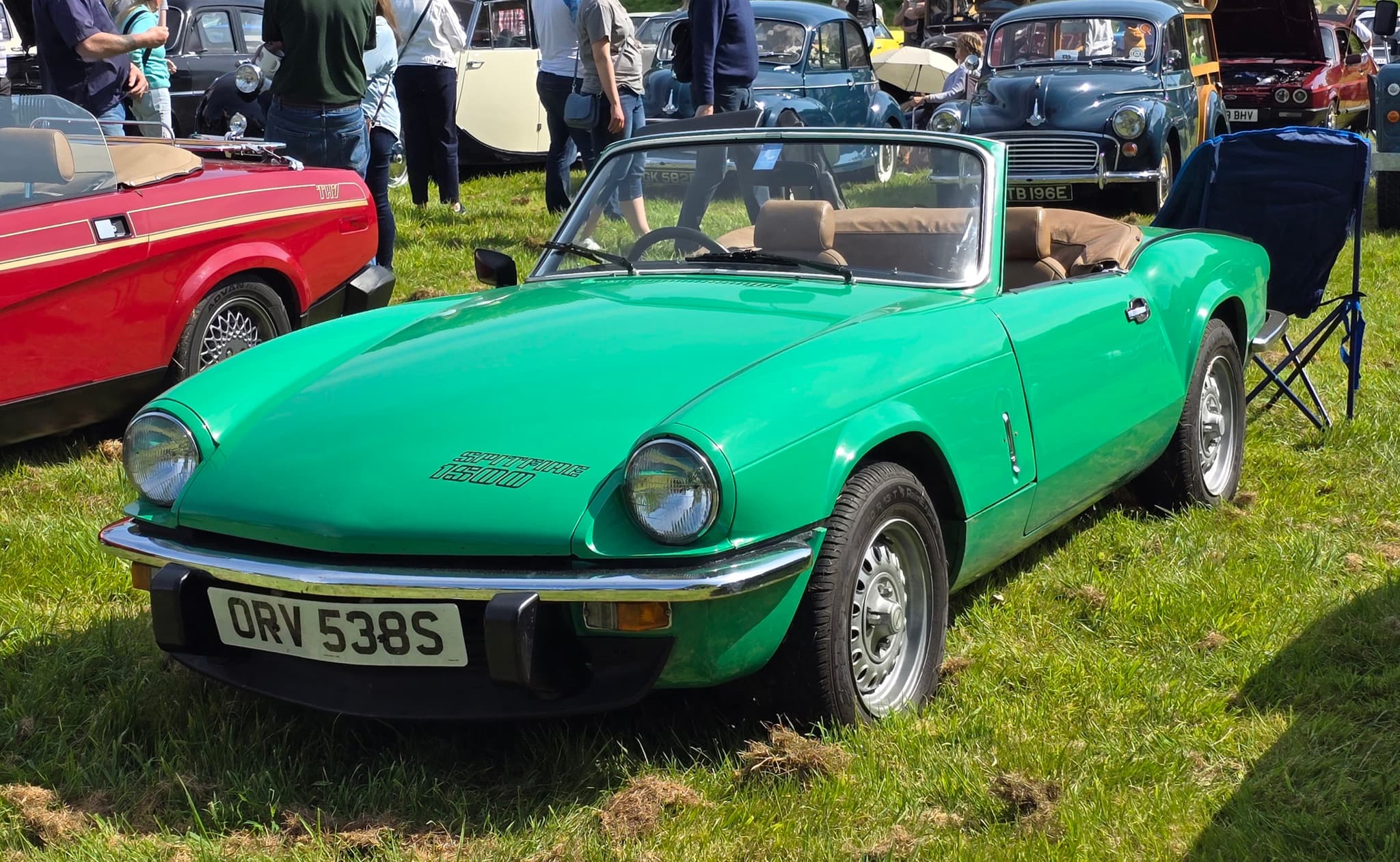 A bright green Spitfire 1500 with tan seats and its hood folded, on a busy show field. Opens a larger view