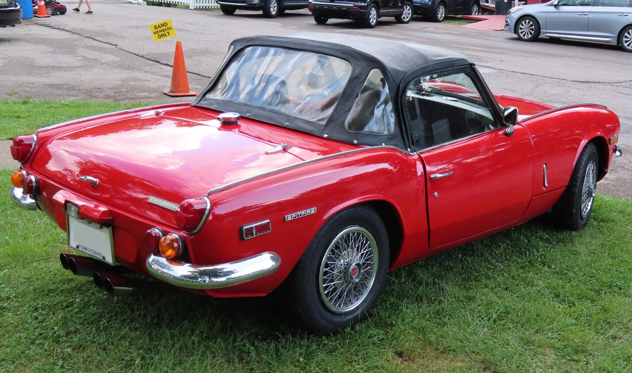 A red Spitfire Mk III with its black hood up, seen from behind on grass, with a red side-marker reflector. Opens a larger view
