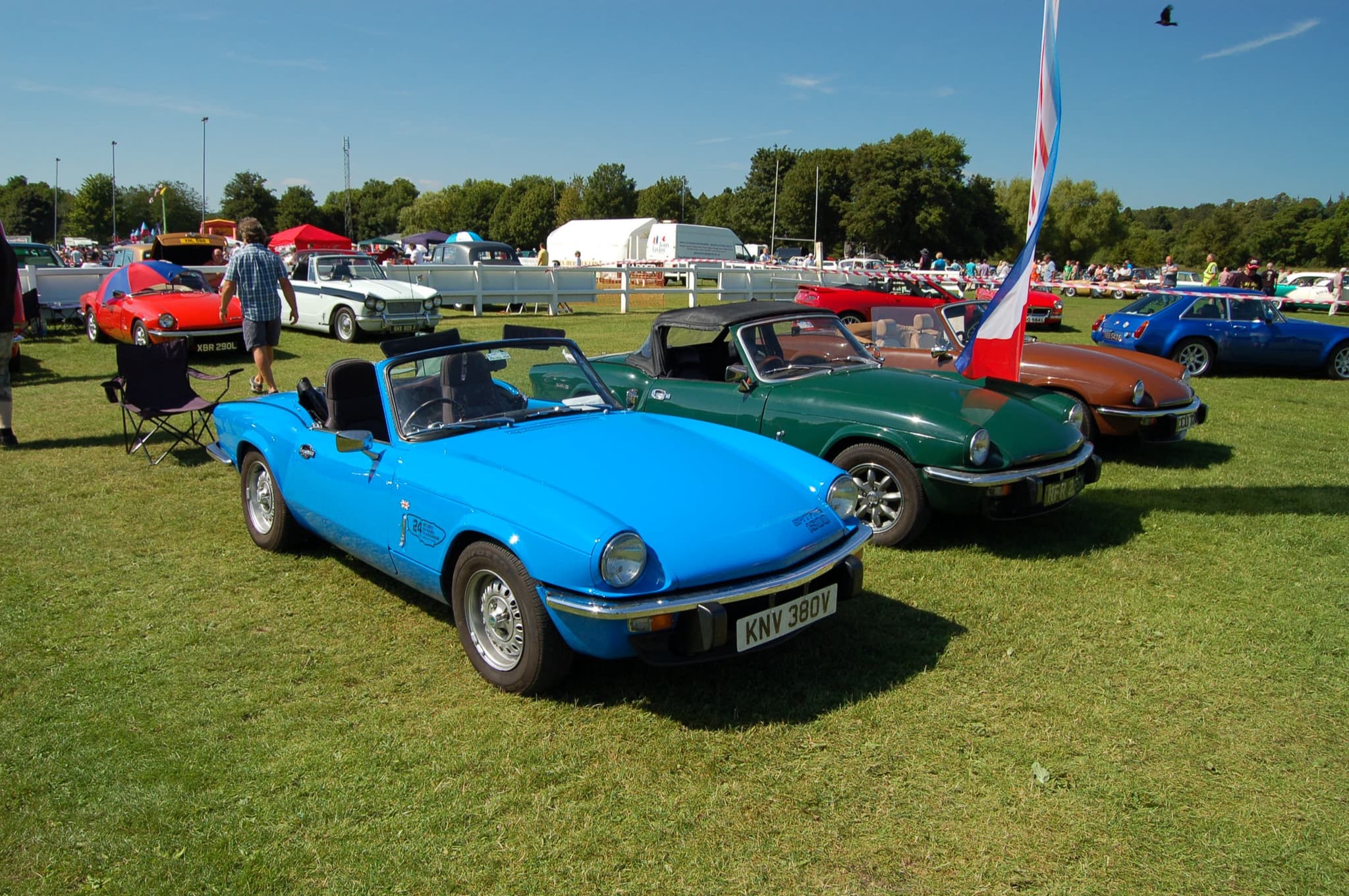 A bright blue Spitfire 1500 parked in front of a dark green and a brown Spitfire on grass.