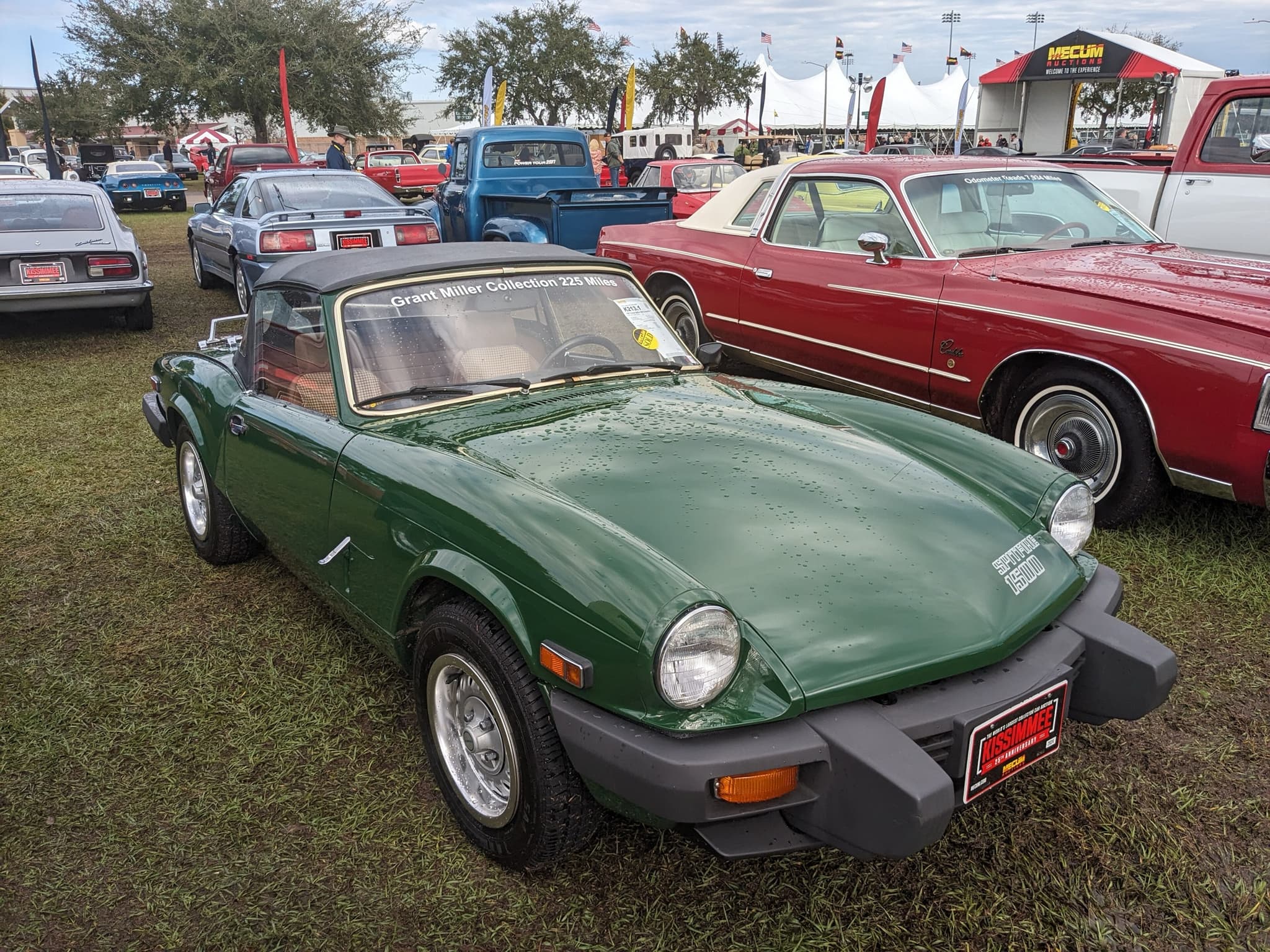 A dark green Spitfire 1500 with its hood up and black rubber bumpers, parked on wet grass.