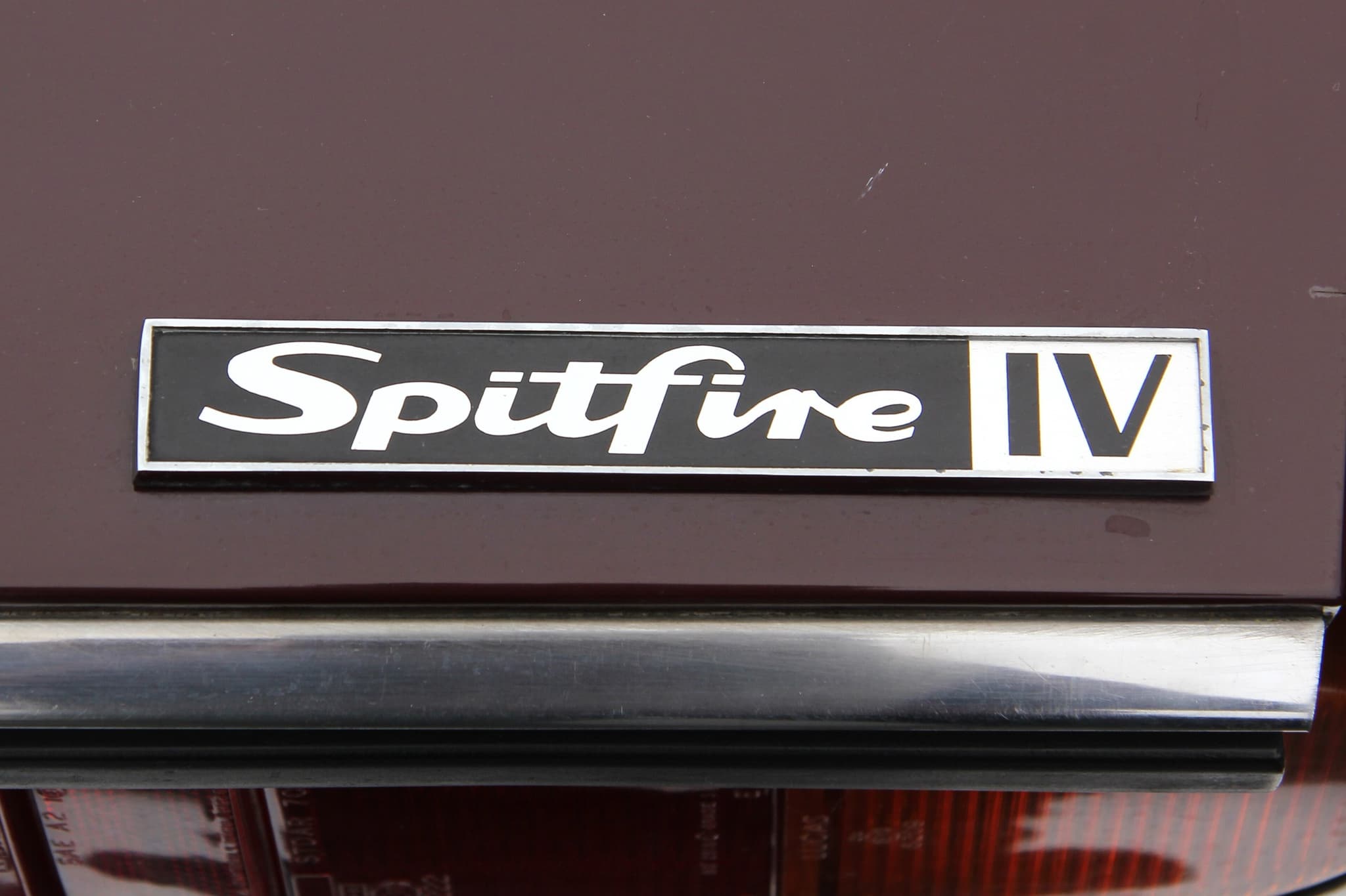 A black and chrome 'Spitfire IV' badge on a maroon boot panel above a chrome bumper. Opens a larger view