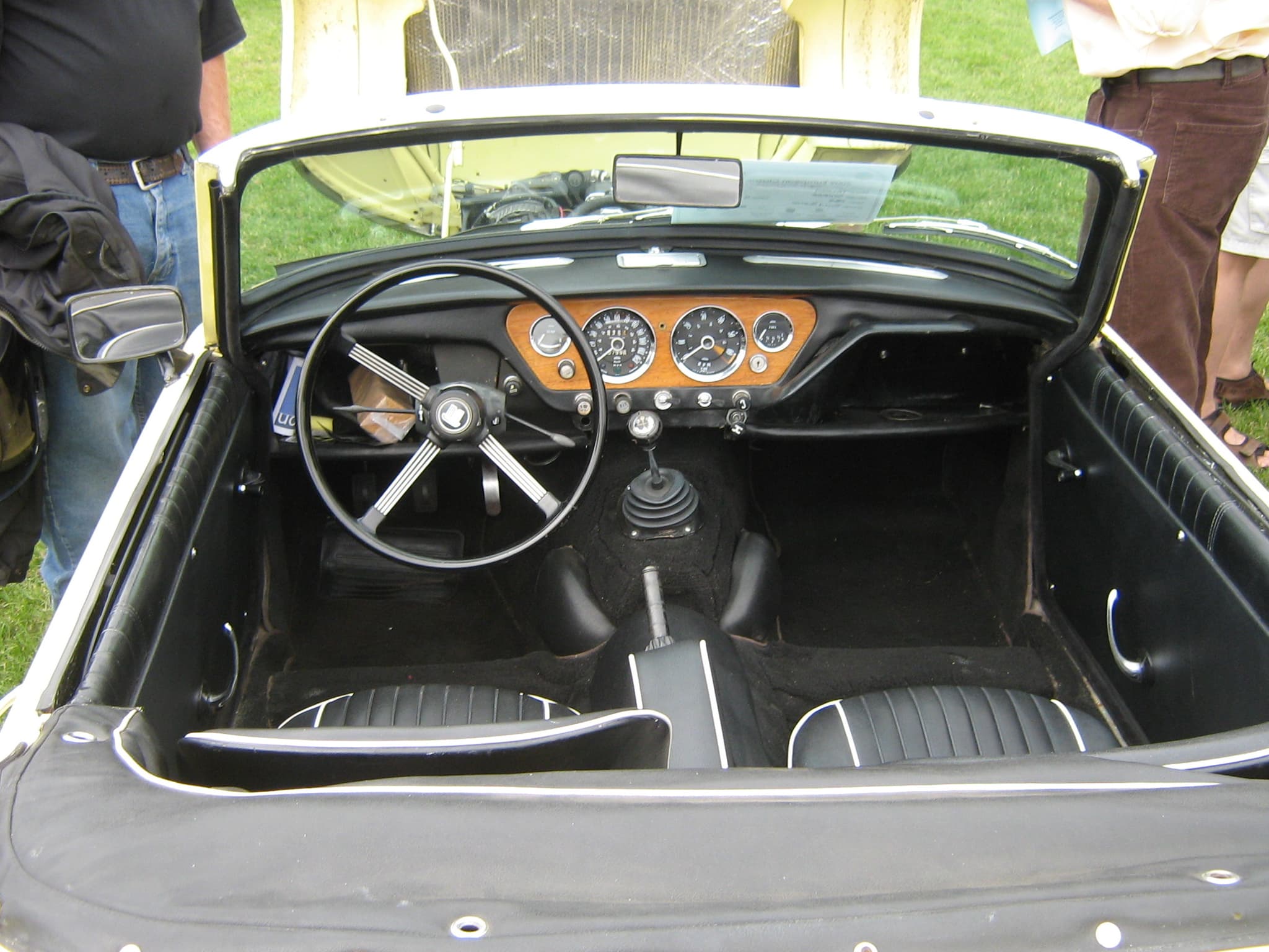 A Spitfire Mk III cockpit from above: centre wood instrument panel, four-spoke wheel, black seats and carpet. Opens a larger view