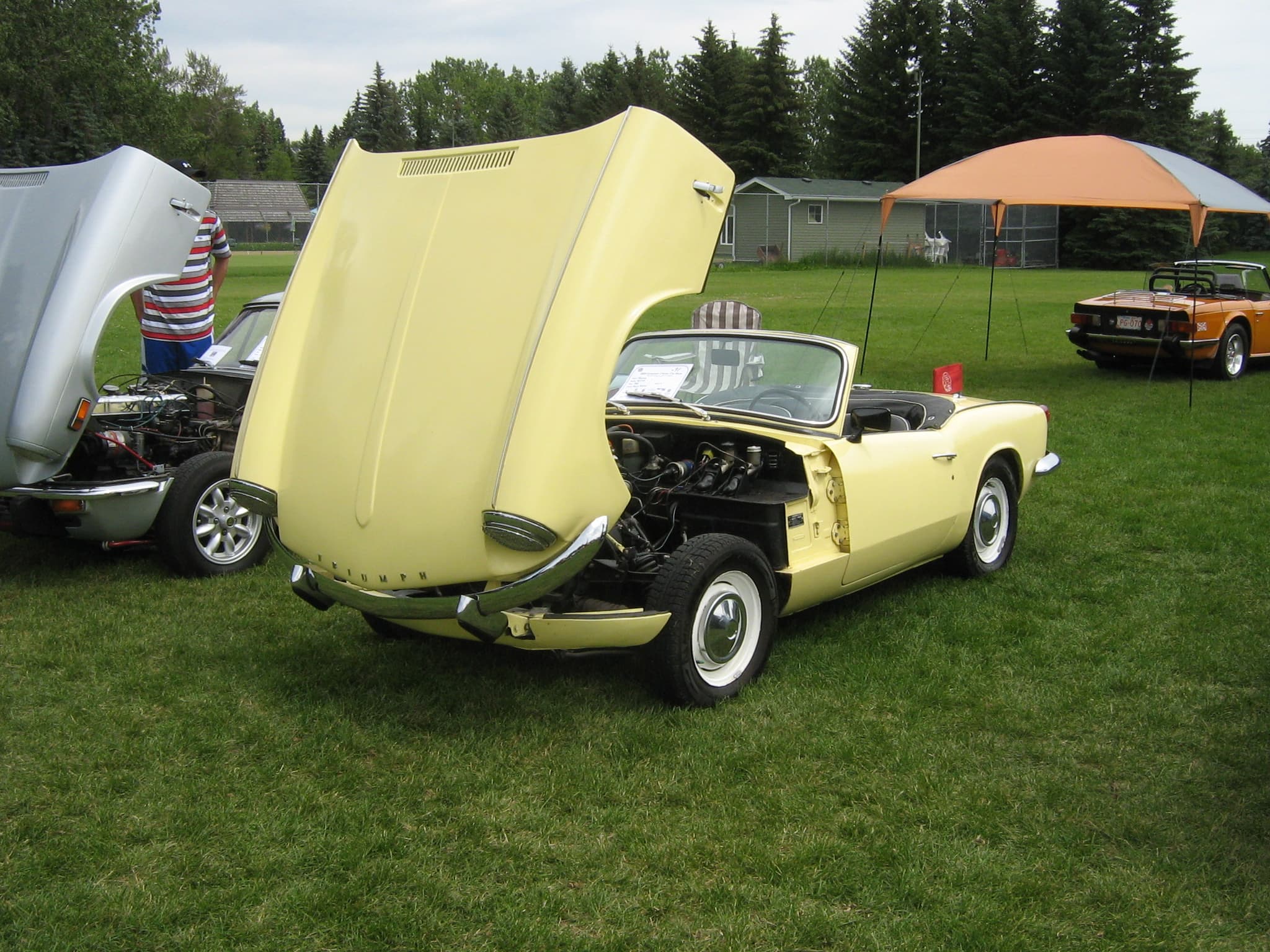 A pale yellow Spitfire Mk III with its whole bonnet tipped forward, showing the engine, on a show field.