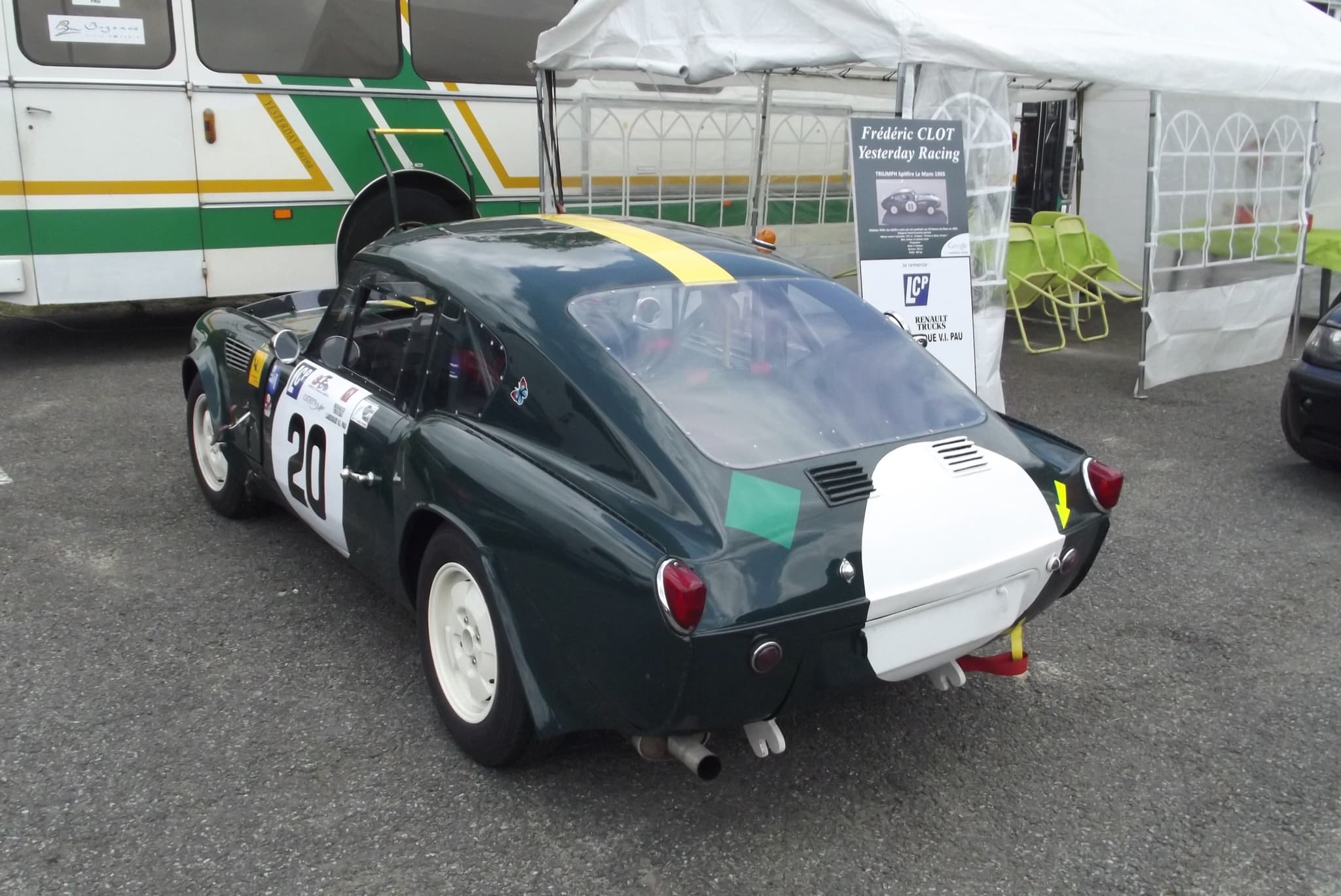 The tail of a dark green fastback Spitfire race car, white tail panel and number 20, in a paddock. Opens a larger view