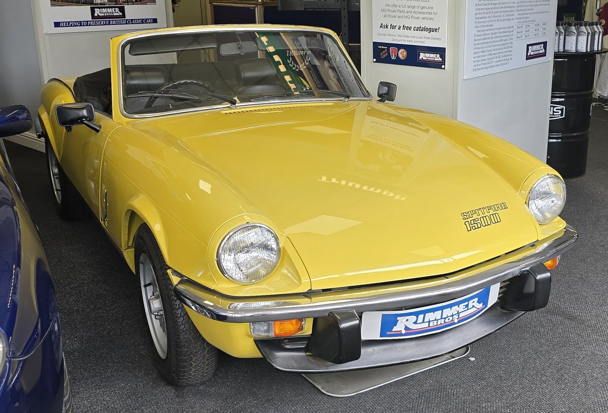 A bright yellow Spitfire 1500 with the hood folded, displayed indoors on a carpeted showroom floor.