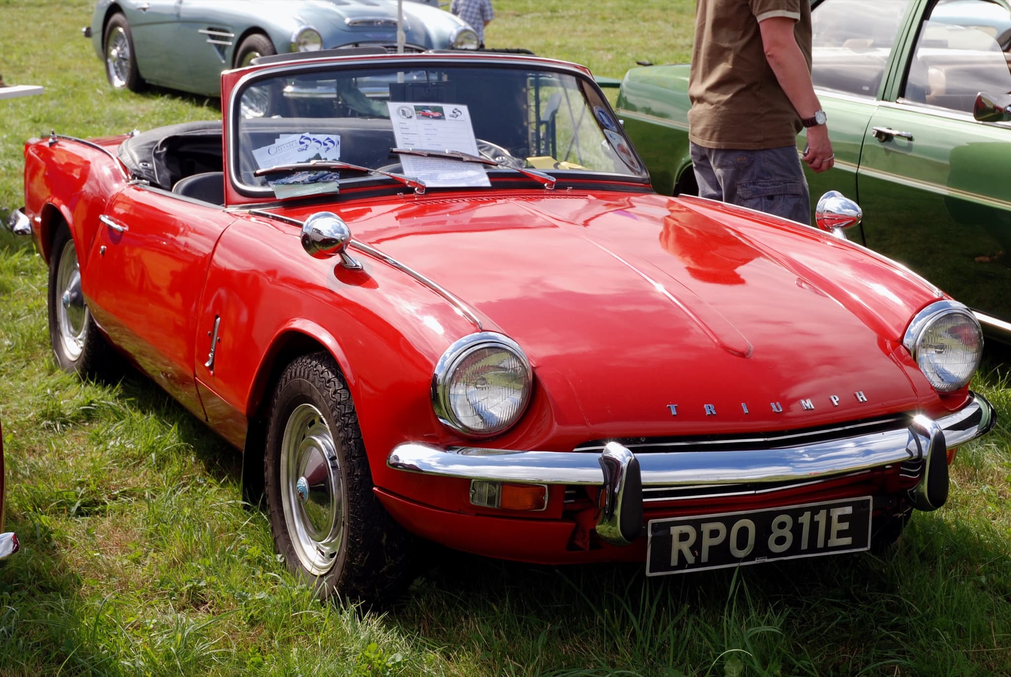 A red Spitfire Mk III with wing mirrors and steel wheels, its hood folded, on a sunny show field. Opens a larger view