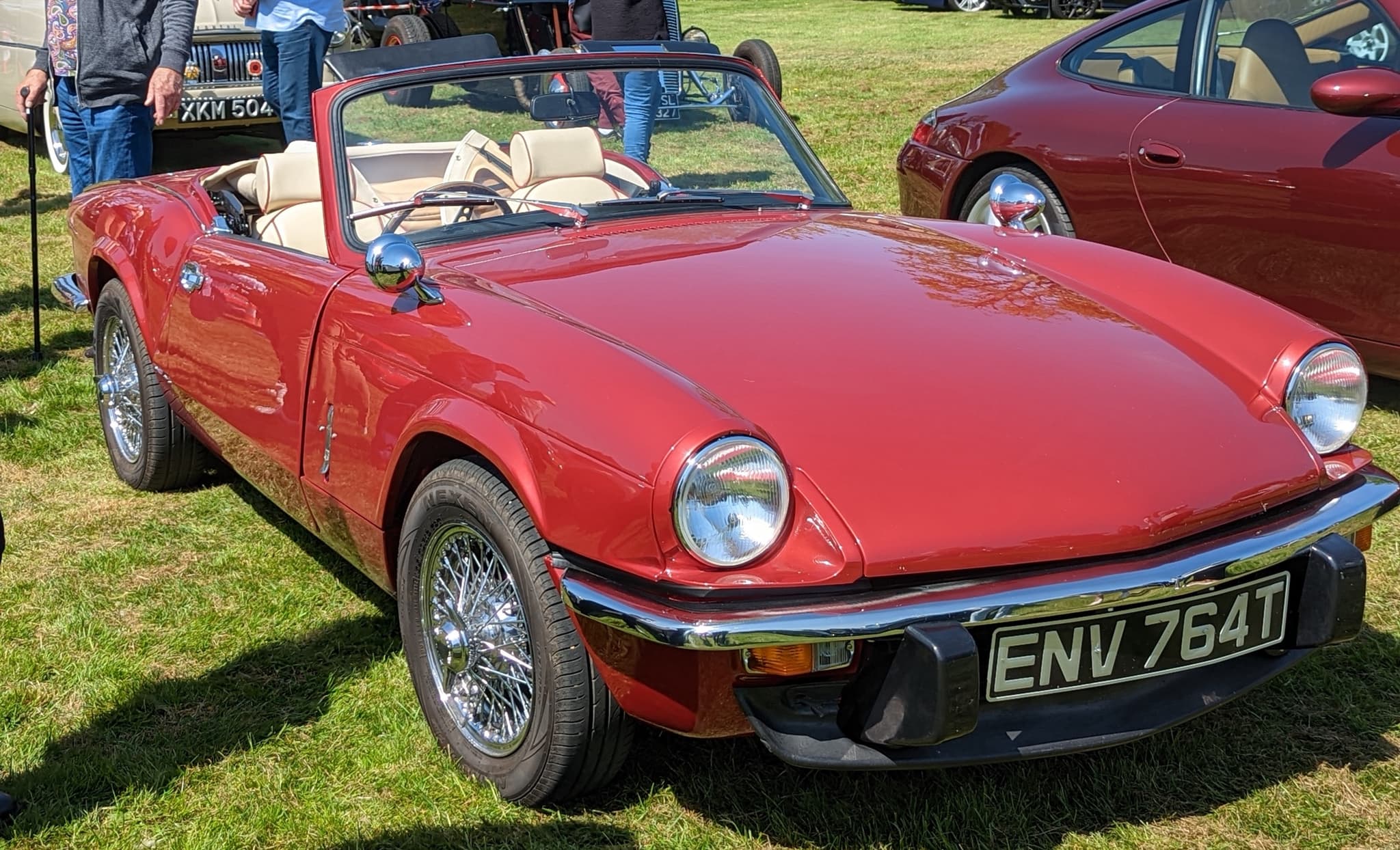 A red Spitfire in the Mk IV body with its hood folded, chrome wire wheels and black bumper under-riders on a sunny show field. Opens a larger view
