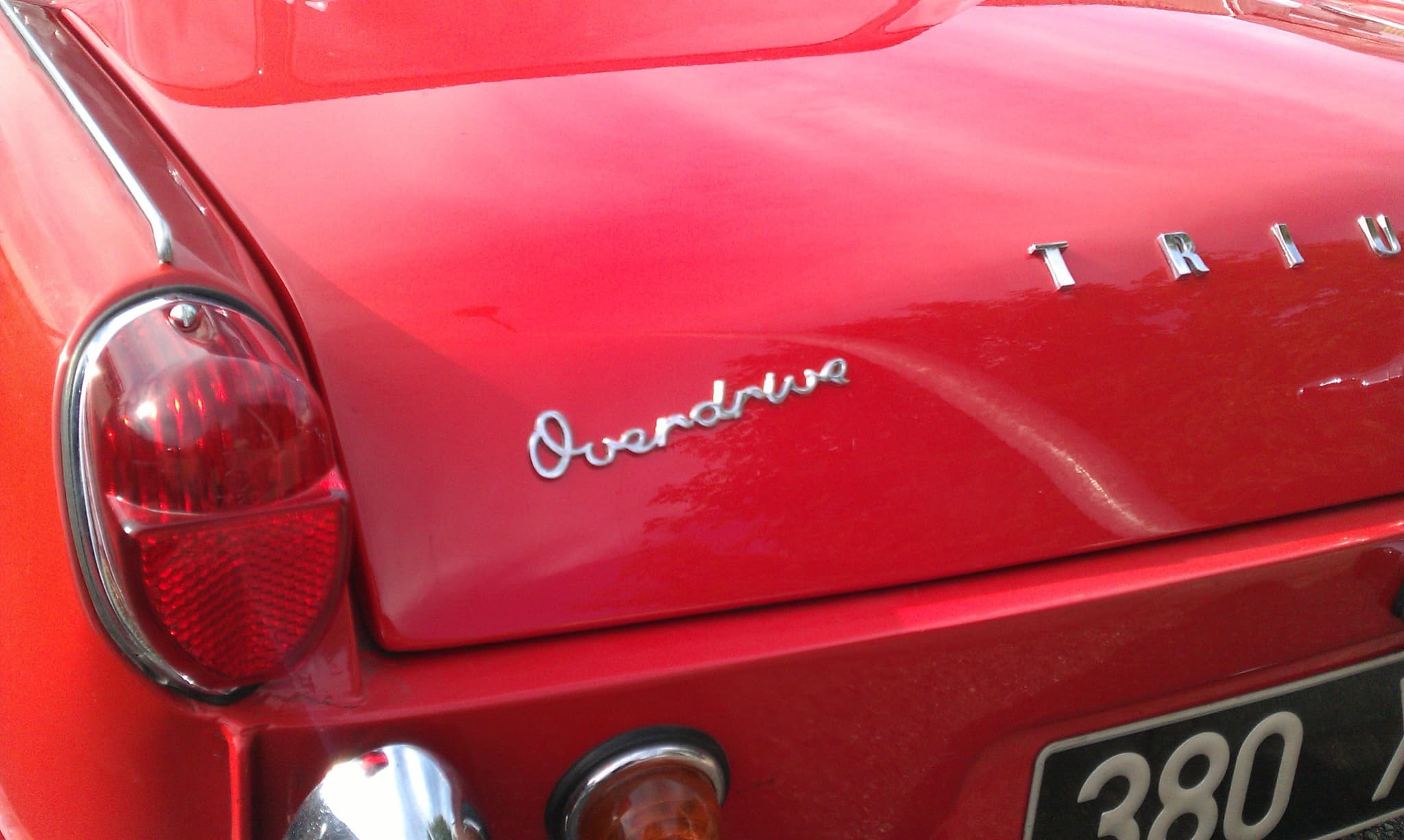 Chrome Overdrive script on the boot lid of a red Spitfire, beside its tall rear lamp. Opens a larger view