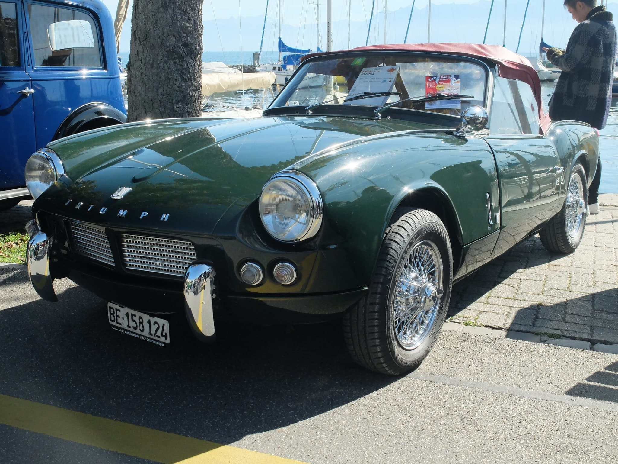 A dark green Spitfire 4 with a maroon hood and wire wheels on a lakeside quay by a marina. Opens a larger view