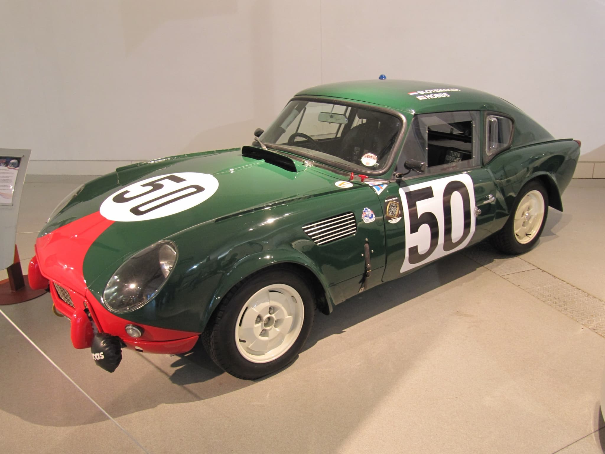 A green Le Mans Spitfire fastback replica with a red nose and race number 50 on a museum floor. Opens a larger view