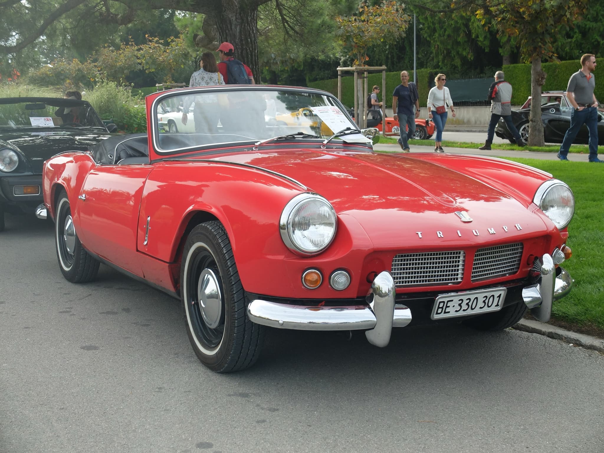 A red Spitfire 4 with whitewall tyres and its hood stowed, parked on a road beside a lawn. Opens a larger view