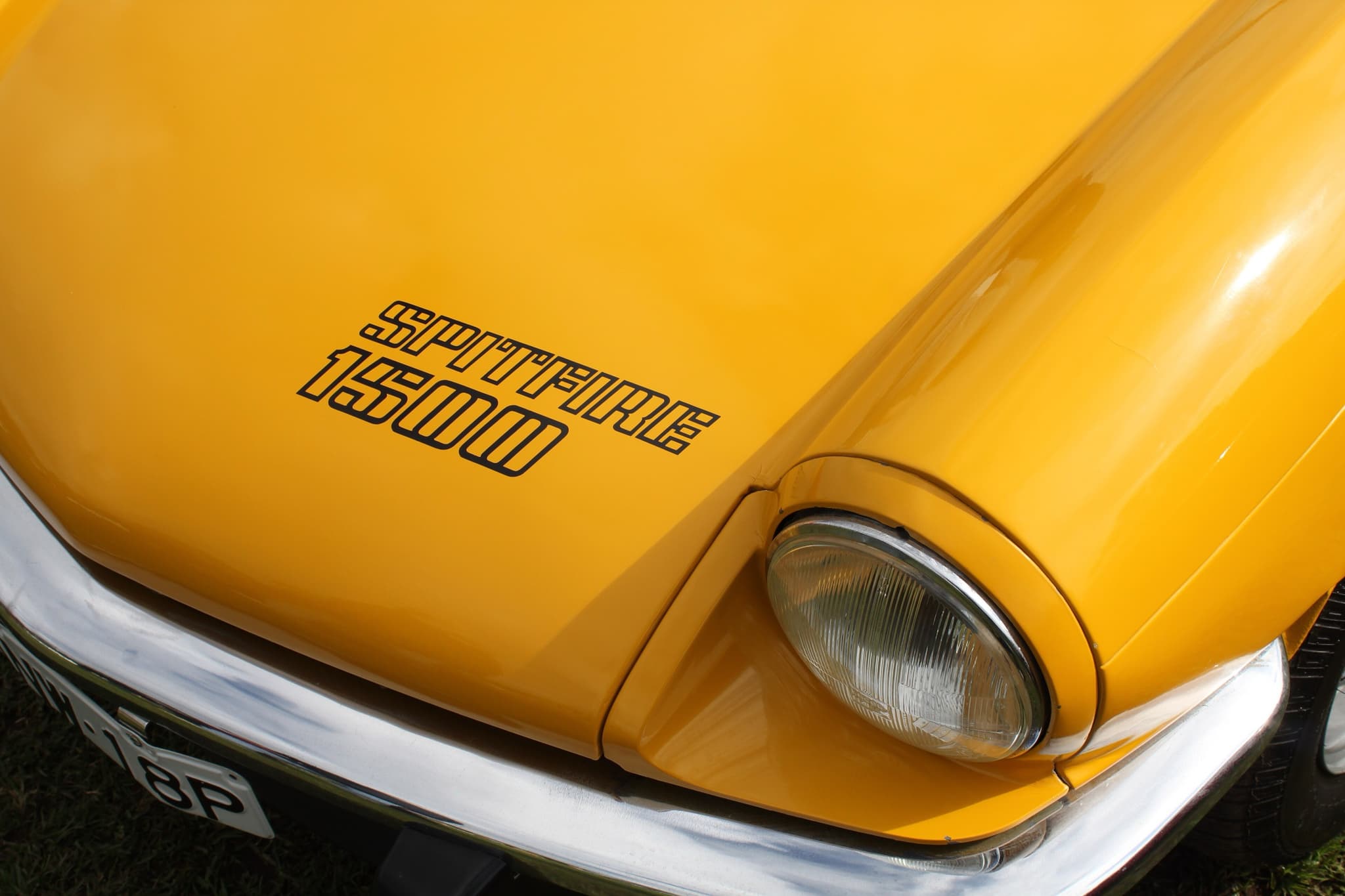 A black SPITFIRE 1500 decal on a yellow bonnet, beside the headlamp and above the chrome bumper. Opens a larger view