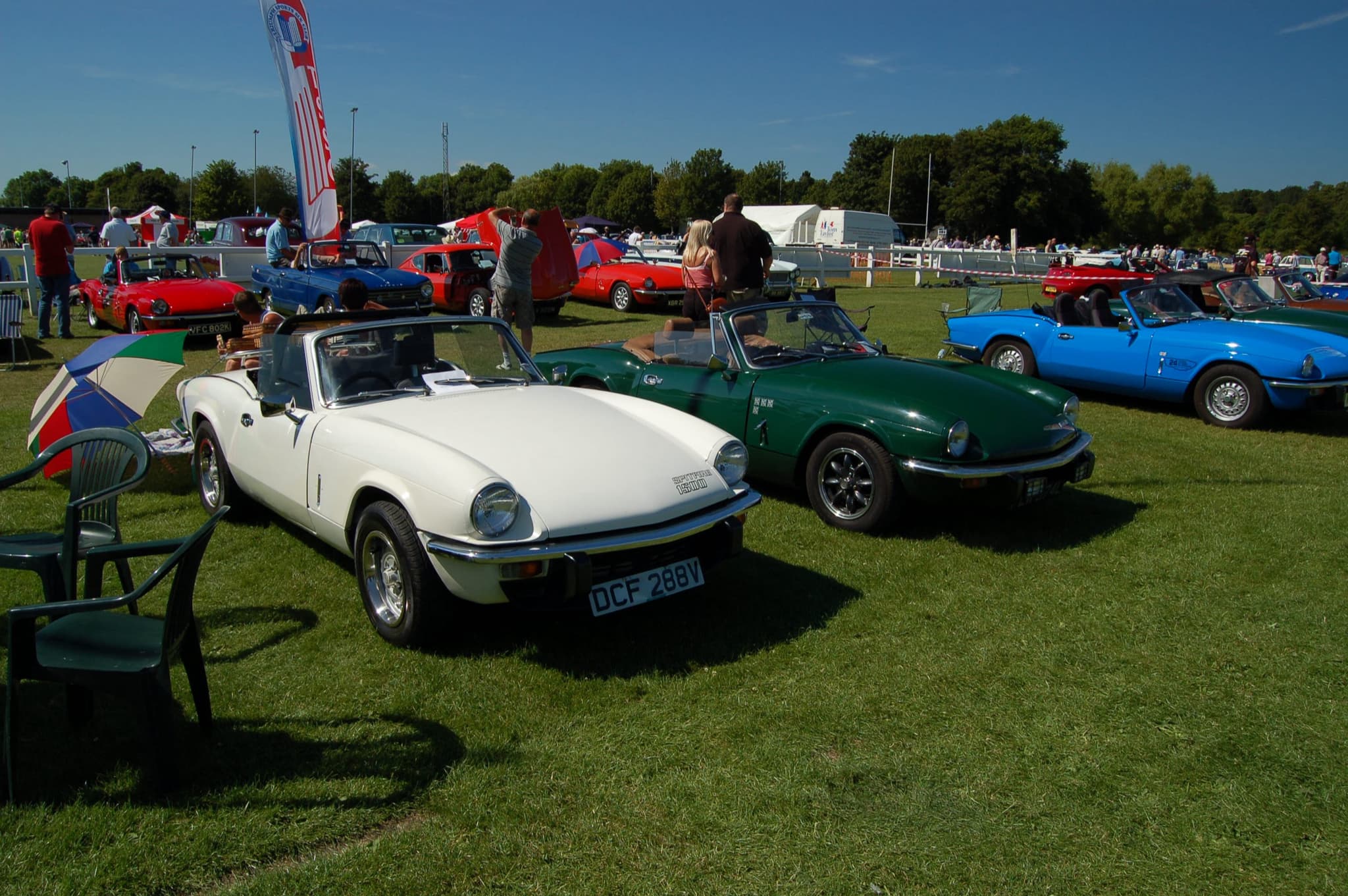 A white Spitfire 1500 in front of dark green and bright blue Spitfires on a sunny show field. Opens a larger view