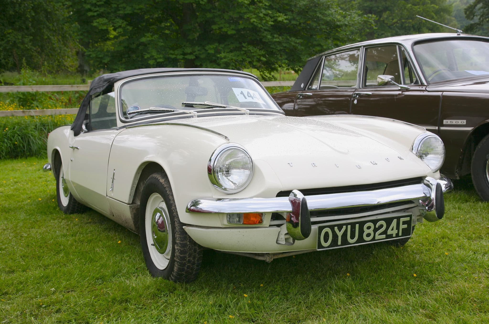 A white Spitfire Mk III with its black hood up and chrome bumper across the grille, on a show-field lawn.