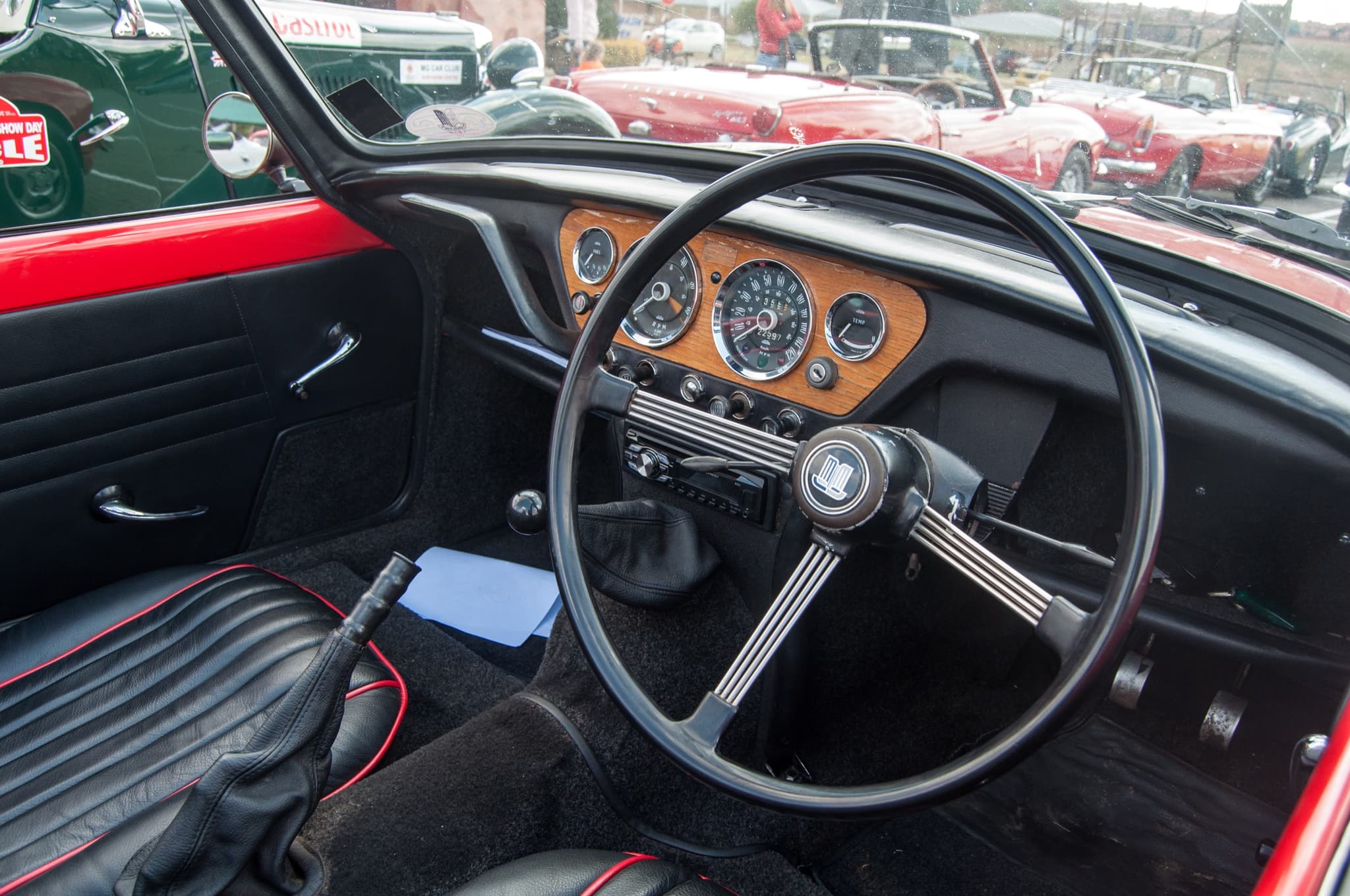 A Spitfire cockpit from the passenger door: wood instrument panel ahead of the driver, large steering wheel, black seats. Opens a larger view