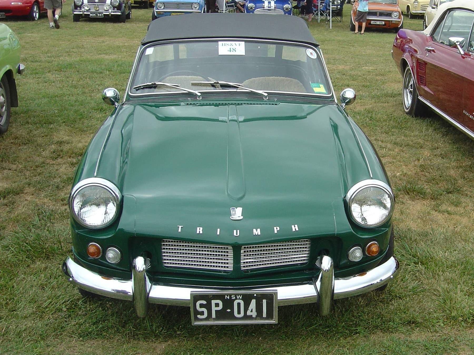 A dark green Spitfire 4 with its black hood up, square on from the front on a show field.