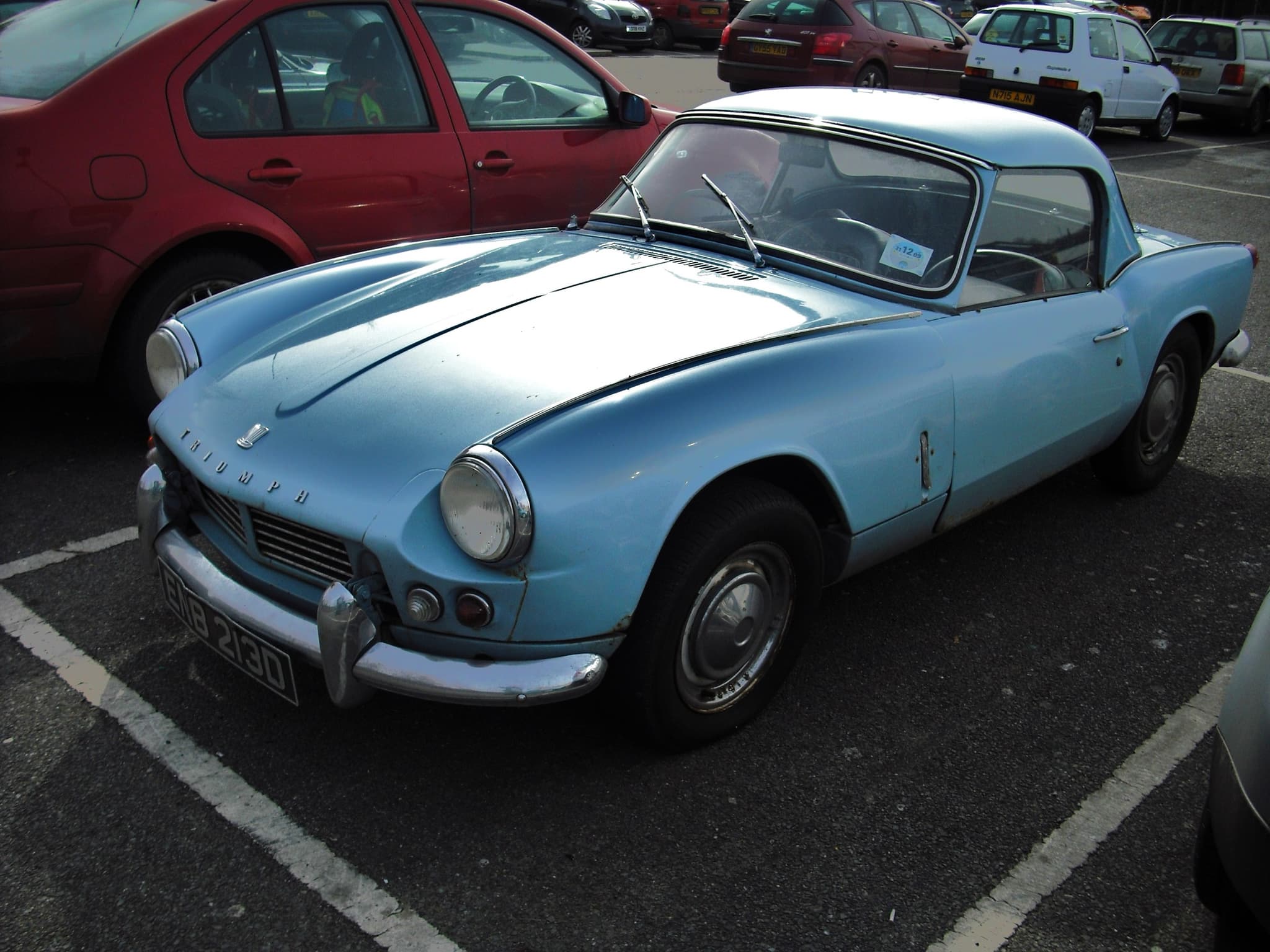 A pale blue Spitfire 4 Mk II with a matching hardtop, parked in a car park bay. Opens a larger view