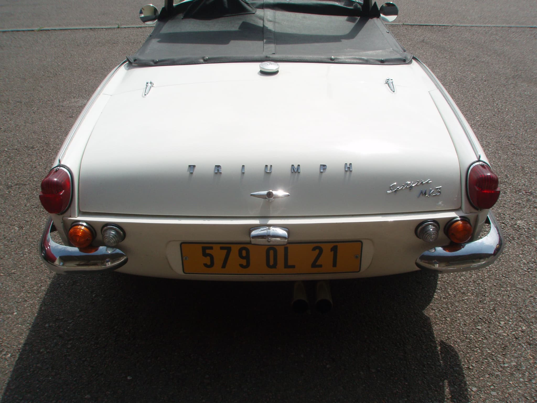 The round tail of a white Spitfire Mk III with its hood folded, seen from behind on tarmac.