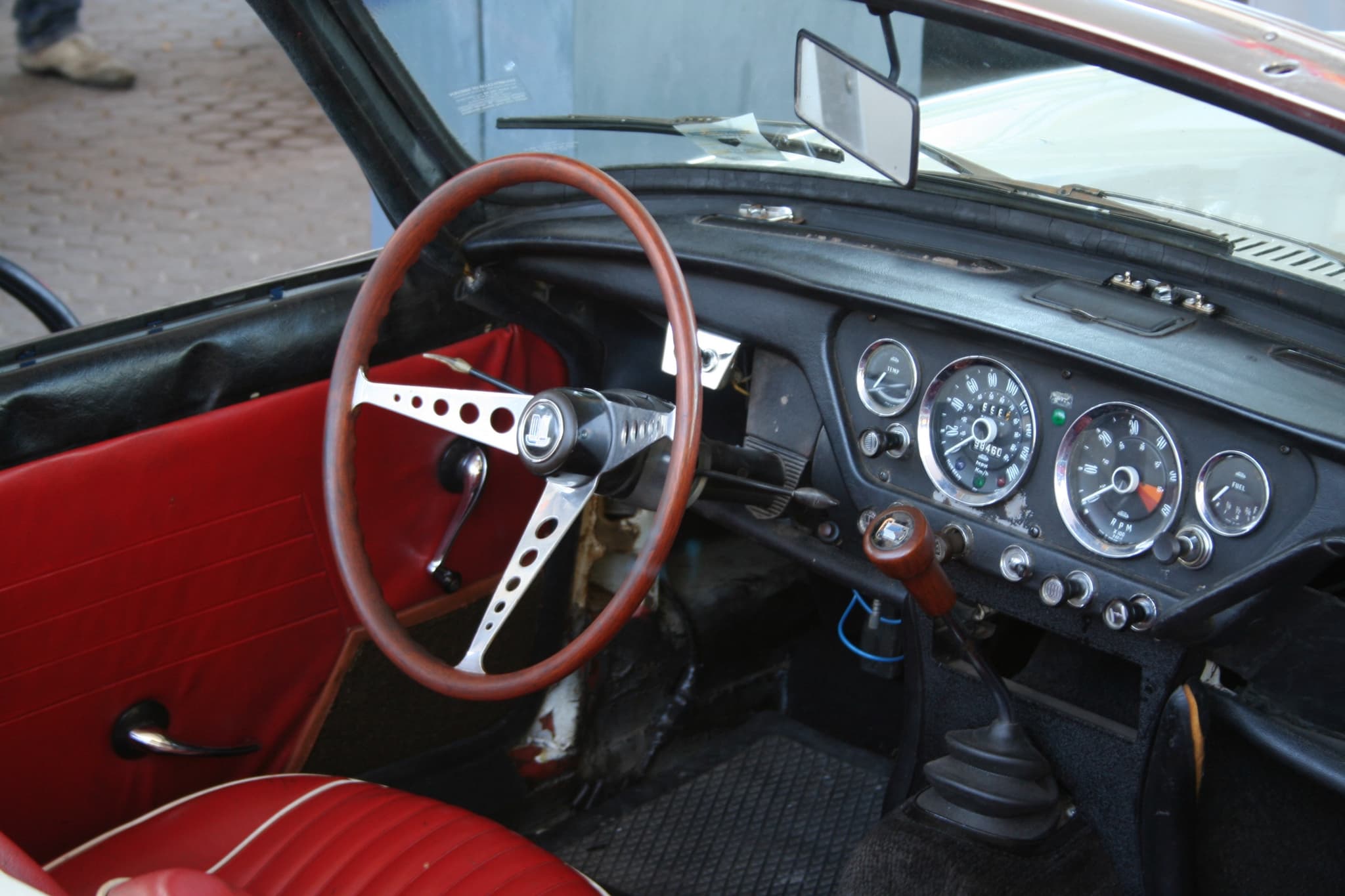 An early Spitfire's cockpit with centre-mounted dials, a drilled wood-rim wheel and red door trim. Opens a larger view