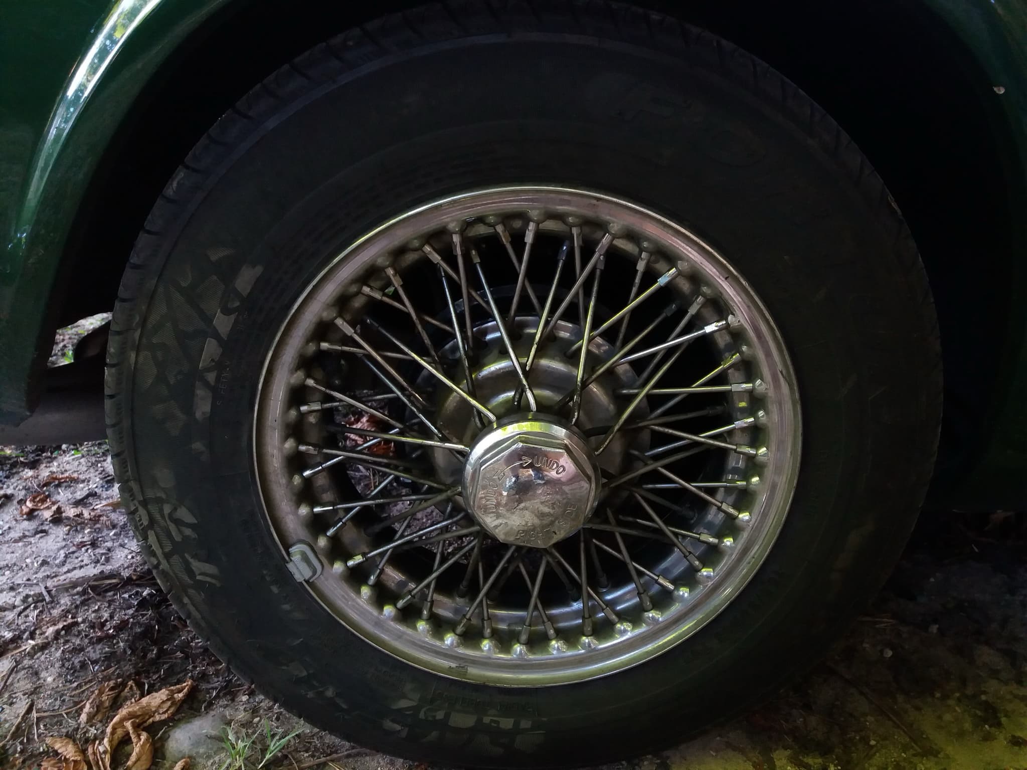Close-up of a chrome wire wheel with an octagonal knock-off nut stamped UNDO, on a green car.