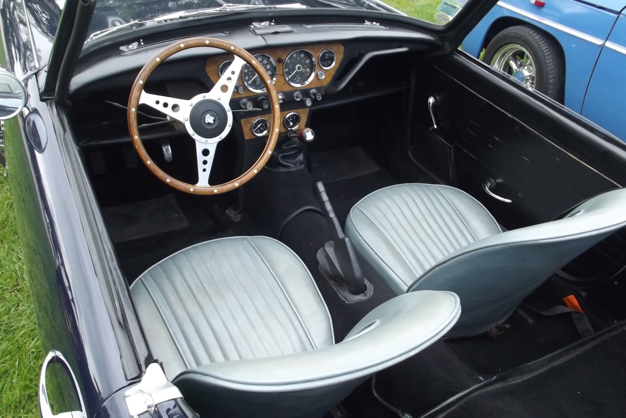 An early Spitfire's cockpit from above, with pale grey seats, central dials and a wood-rim wheel. Opens a larger view