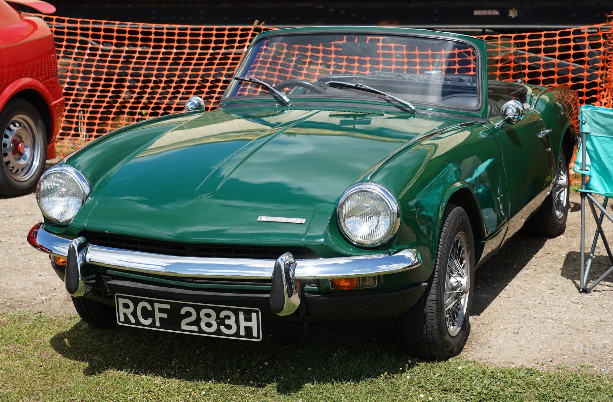 A dark green Spitfire Mk III with wire wheels and its hood folded, in front of orange safety fencing. Opens a larger view