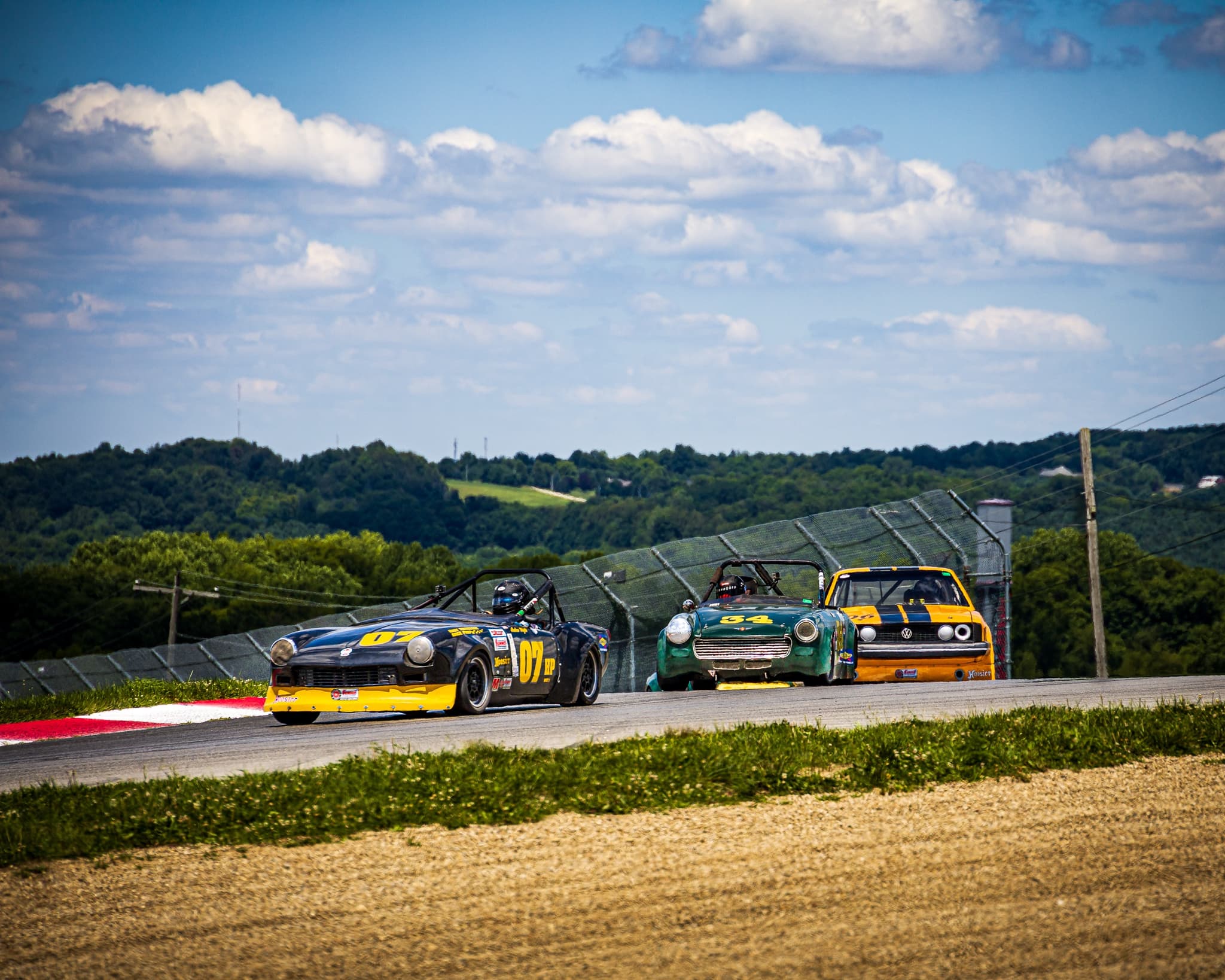 A black Spitfire race car, number 07, leading an MG Midget and a Volkswagen through a bend.