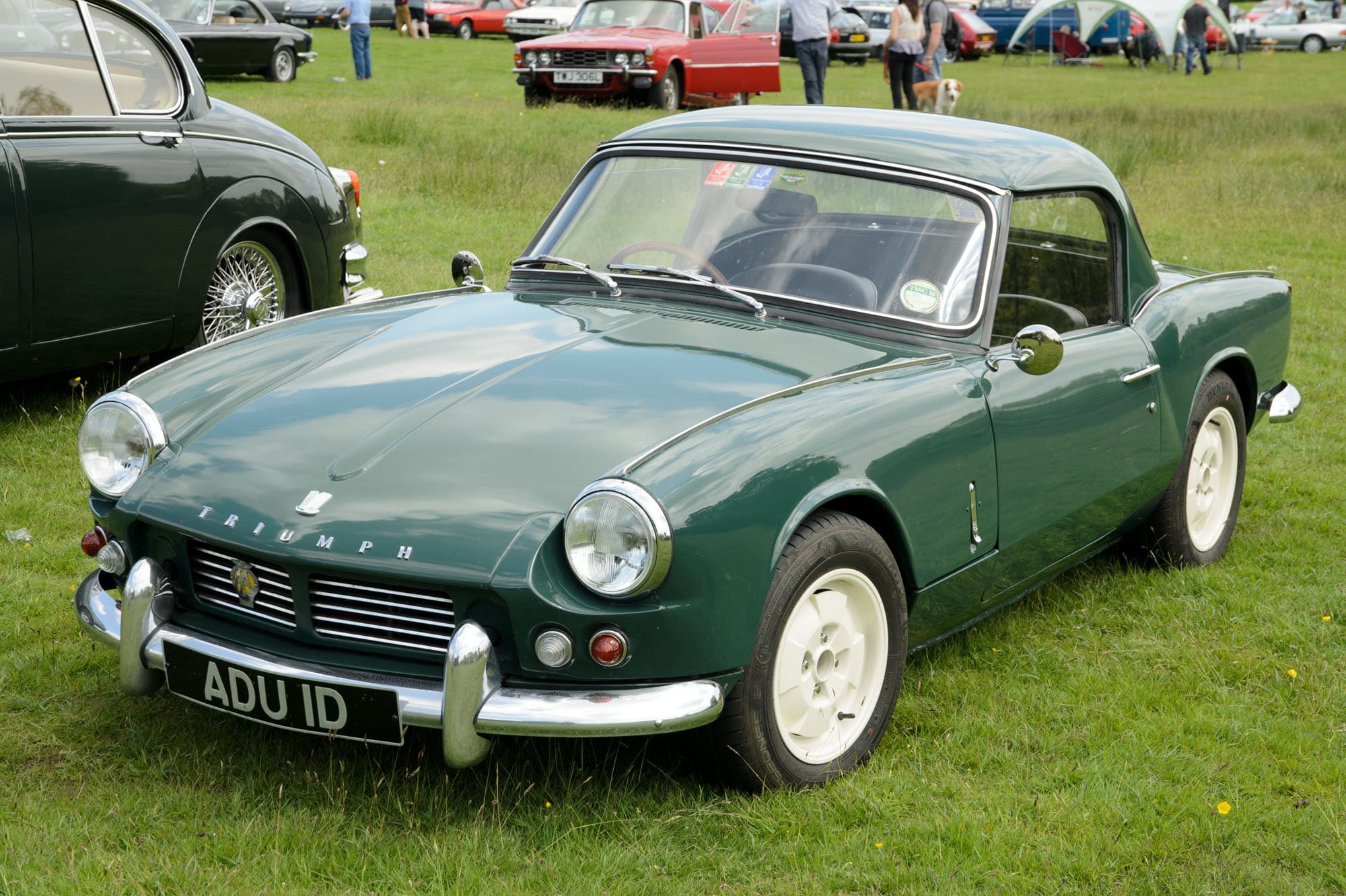 A dark green Spitfire 4 Mk II with a matching hardtop and white wheels on a grass show field. Opens a larger view