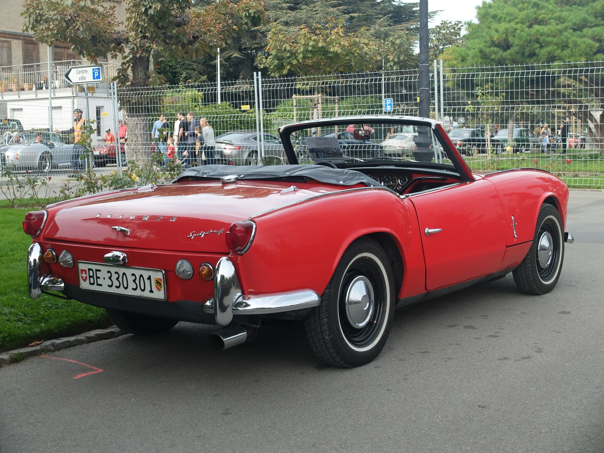 The tail of a red Spitfire 4 with chrome quarter-bumpers and whitewall tyres, parked beside a lawn. Opens a larger view