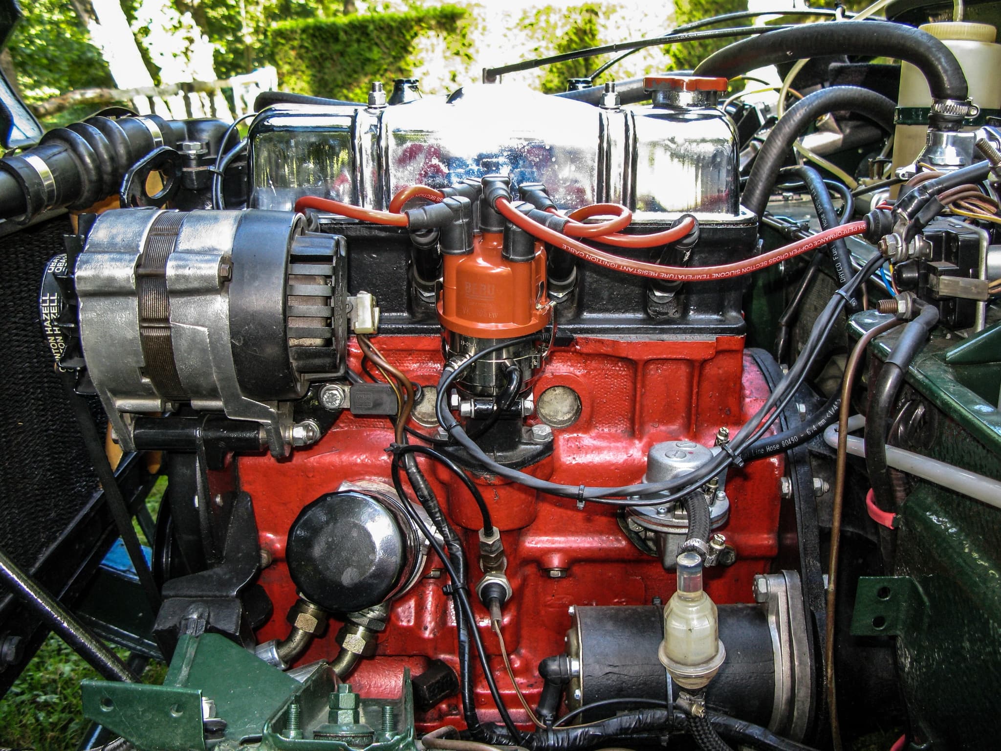 Close view of a Spitfire engine with a polished rocker cover, red block, orange distributor cap and alternator.