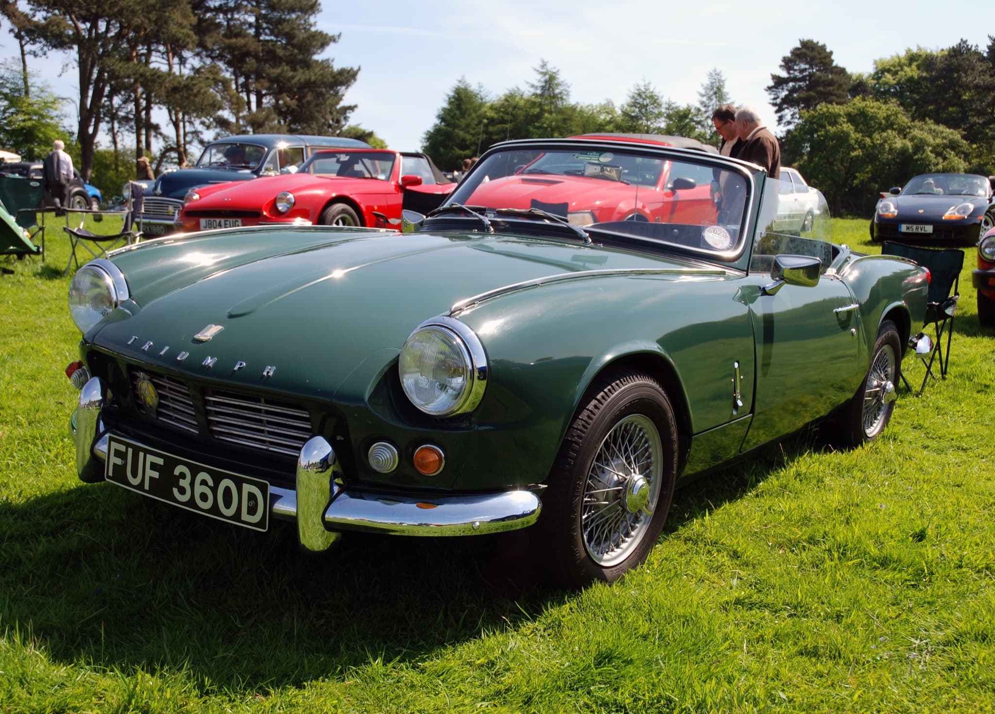 A dark green Spitfire 4 Mk II with wire wheels and its hood folded, on a lawn among other classics. Opens a larger view