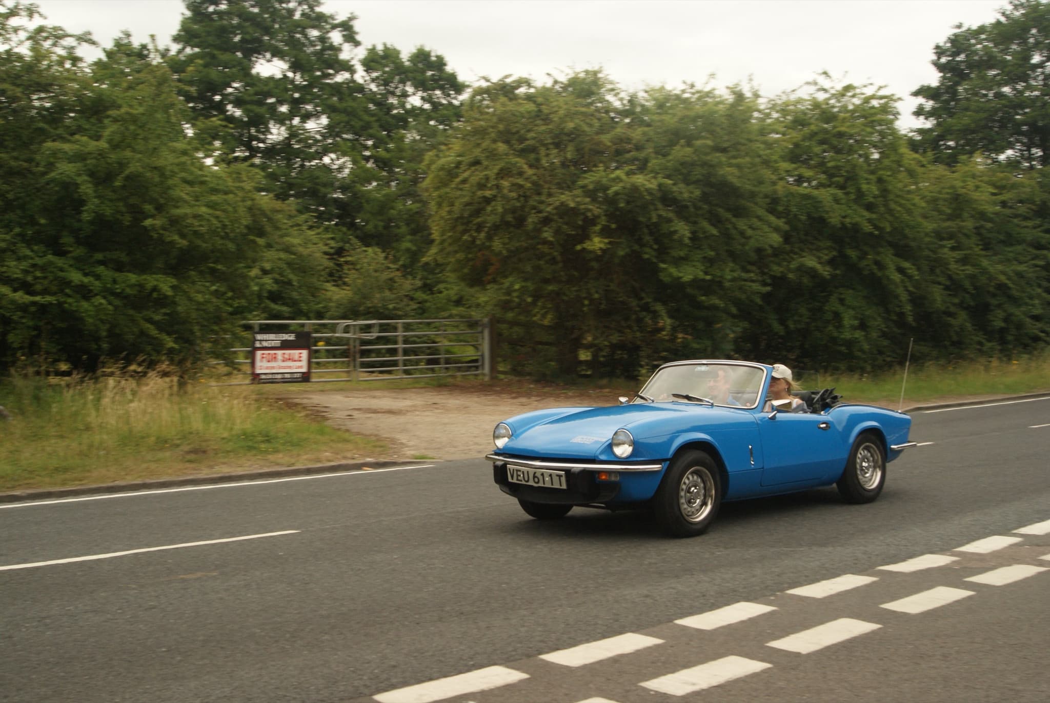 A blue Spitfire 1500 with its hood down driving along a tree-lined country road.