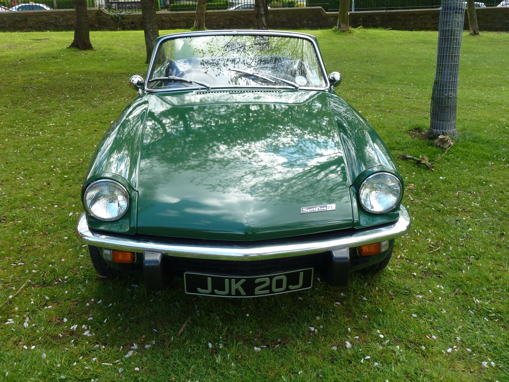A dark green Spitfire Mk IV with the hood down, square on from the front on park grass under trees.
