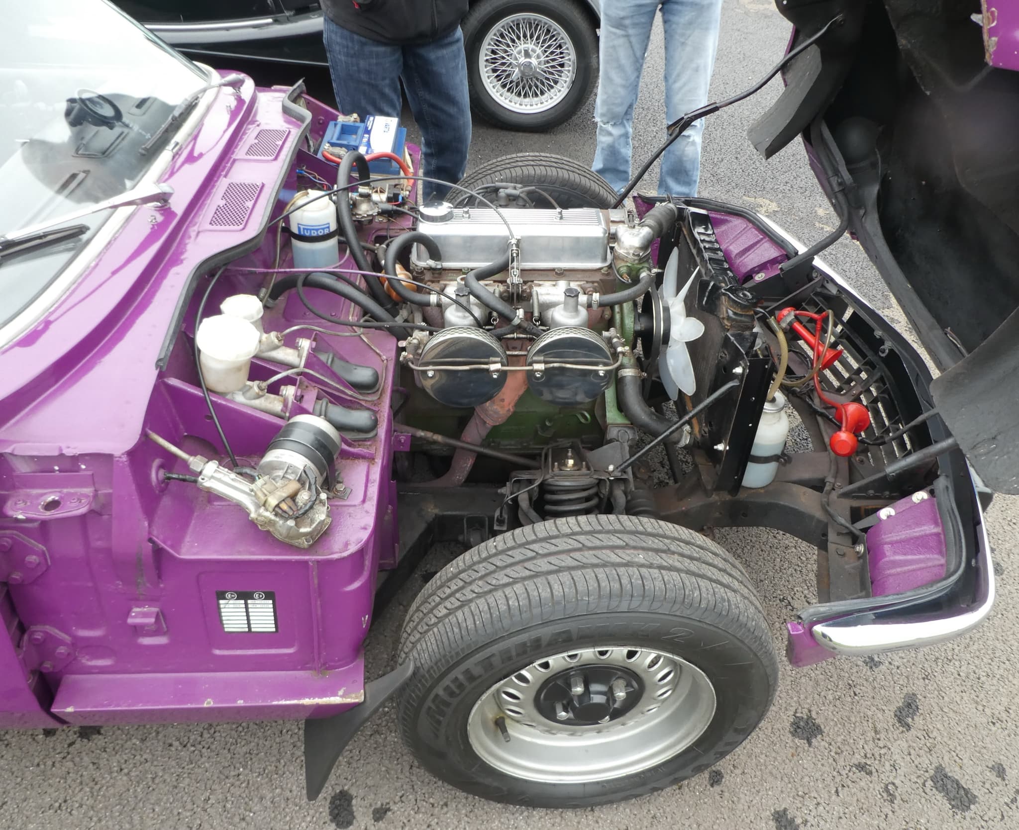 A purple Spitfire with its bonnet tipped forward, showing the engine, twin chrome air filters, coil spring and front wheel. Opens a larger view